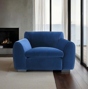 Karl Royal Blue Contemporary Chenille Fabric Chair Blue armchair in a modern living room with a fireplace and large windows.