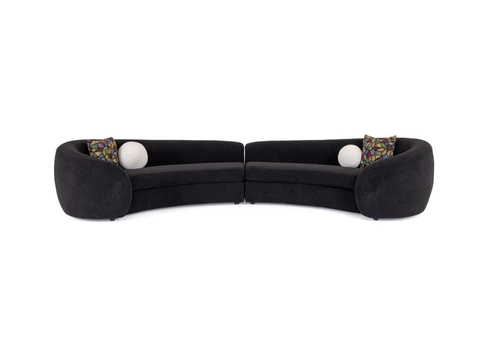 Kilmer Black Fabric Curved Modern Sectional Sofa A modern curved black sectional sofa in a styled living room, paired with round black coffee tables, a patterned rug, and a large framed abstract art print on the wall.
