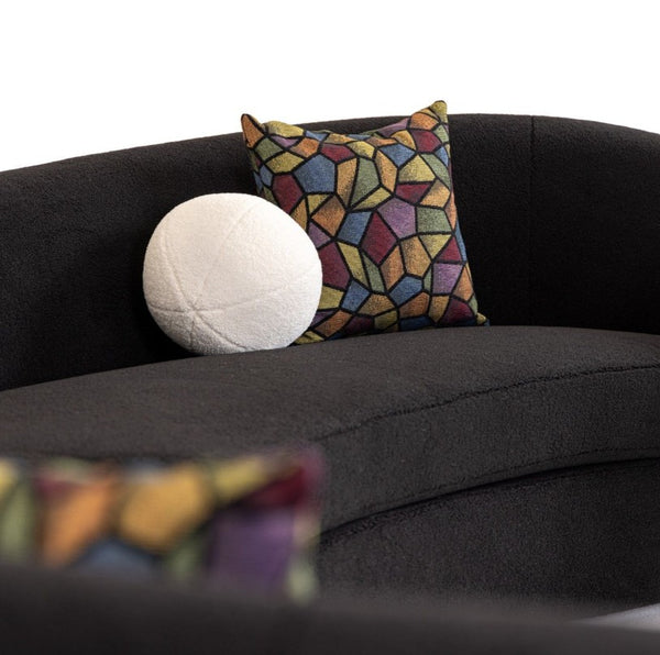 Kilmer Black Fabric Curved Modern Sectional Sofa A dark charcoal gray upholstered sofa with two decorative throw pillows: a white textured round pillow and a square pillow featuring a multicolor geometric mosaic pattern in yellow, blue, red, and green.