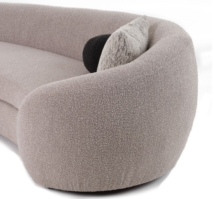 Kilmer Gray Fabric Curved Modern Sectional Sofa A modern curved light gray sofa in a minimalist living room setting, styled with black accent pillows, a patterned area rug, low black coffee tables, and a framed abstract art print on the wall.