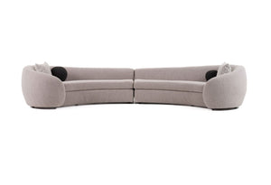 Kilmer Gray Fabric Curved Modern Sectional Sofa A curved modular sofa in a light taupe-beige fabric, featuring two separate seat sections, low rounded armrests, and two black circular accent pillows, shown against a plain white background.