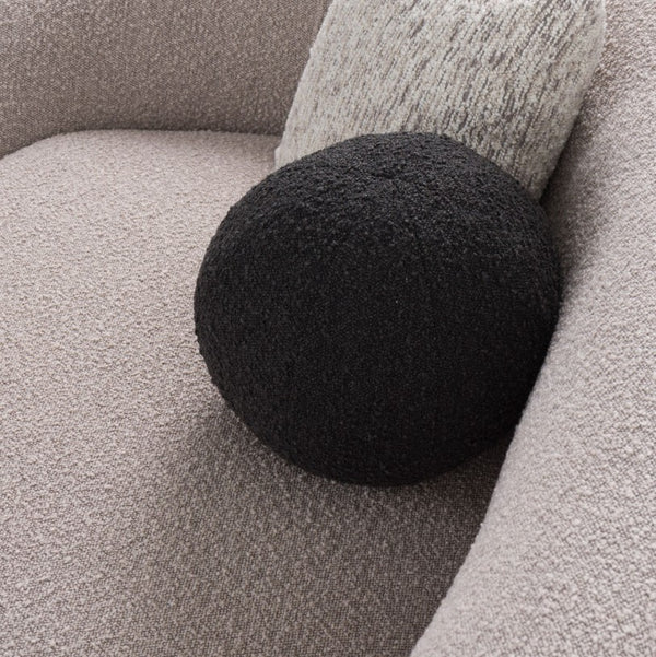 Kilmer Gray Fabric Curved Modern Sectional Sofa A round black textured throw pillow resting on a light beige boucle sofa next to a gray textured pillow.