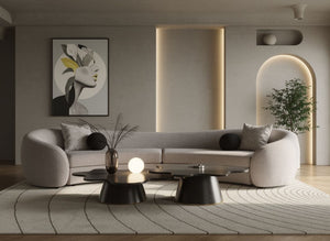 Kilmer Gray Fabric Curved Modern Sectional Sofa A modern curved light gray sofa in a minimalist living room setting, styled with black accent pillows, a patterned area rug, low black coffee tables, and a framed abstract art print on the wall.