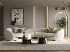 Kilmer Off White Fabric Curved Modern Sectional Sofa A modern curved white sofa in a minimalist living room setting, styled with neutral beige and brown pillows, a black coffee table, and a textured rug.