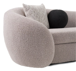 Close-up of a rounded upholstered armchair in a textured boucle fabric, shown with two decorative pillows against a plain white background.