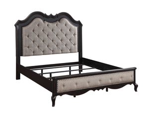 Lesley Button Tufted Camel Back Headboard Bed A dark wood bed frame with a tall, tufted headboard and matching footboard, featuring light beige upholstery and silver nailhead trim, shown on a plain white background.