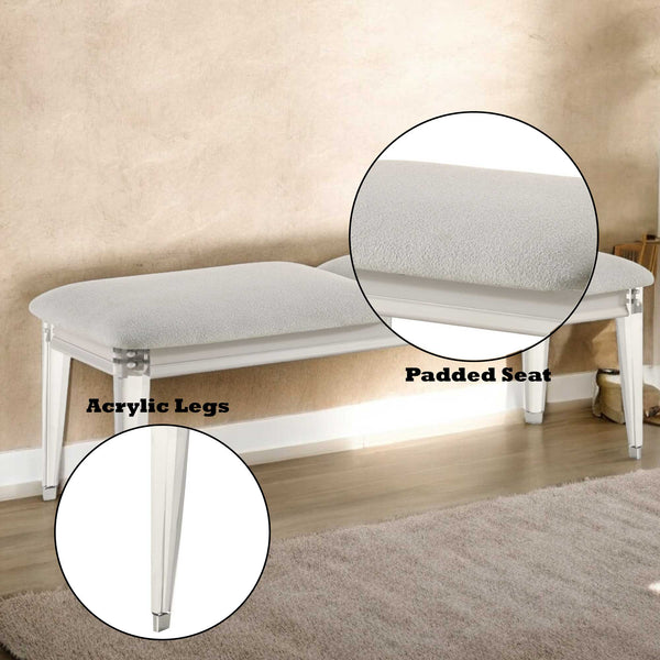 White bench with padded seat and acrylic legs on a wooden floor.