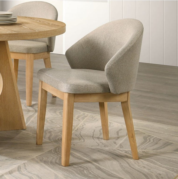 Maeve Organic Modern Oak Finish Dining Chair Dining chair with wooden legs and gray cushioned seat and backrest in a room with a wooden table.