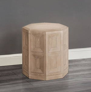 Montague Cross Modern Style Tawny End Table A light natural wood octagonal side stool with a paneled geometric design, shown on a dark gray wood floor against a gray wall.