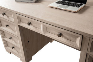 Montague Cross Modern Classic Tawny Executive Desk A light beige wood writing desk with multiple drawers and round metal knobs, shown with a laptop on top against a white background.