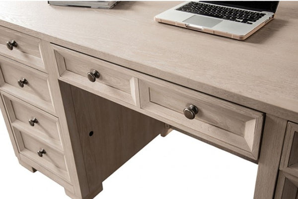 Montague Cross Modern Classic Tawny Executive Desk A light beige wood writing desk with multiple drawers and round metal knobs, shown with a laptop on top against a white background.