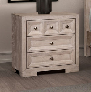 Montague Cross Modern Classic Tawny Nightstand A light gray wood nightstand with three drawers and round metallic knobs, shown in a bedroom setting on a wood floor.
