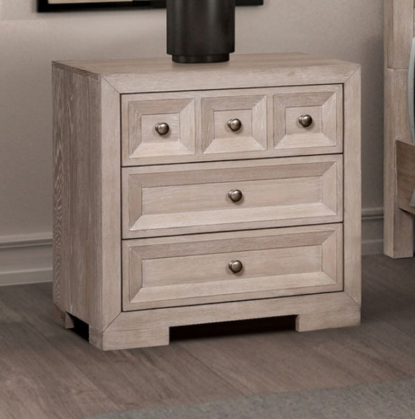 Montague Cross Modern Classic Tawny Nightstand A light gray wood nightstand with three drawers and round metallic knobs, shown in a bedroom setting on a wood floor.
