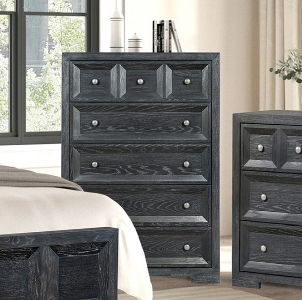 Montague Cross Modern Classic Weathered Black Chest A dark charcoal gray wooden dresser and matching nightstand in a bedroom setting, shown next to a bed with white bedding.