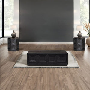 Montague Cross Modern Style Weathered Black Coffee Table A dark wood rectangular coffee table with carved panel details sits on a light rug in a modern living room setting with wood floors, a dark gray accent wall, and matching side tables with lamps.