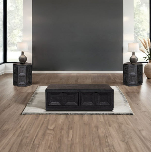 Montague Cross Modern Style Weathered Black End Table A dark wood rectangular coffee table centered on a light rug in a modern living room with wood floors, a dark gray wall, two matching side tables with lamps, and a plant.