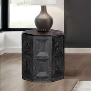 Montague Cross Modern Style Weathered Black End Table Hexagonal side table with textured surface and lamp on top in a room setting.