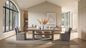 Montague Cross Modern Style Rectangular Dining Table A modern dining room featuring a light wood rectangular table with four upholstered gray chairs, set on a large beige area rug. The room has a high vaulted ceiling, large arched windows with black frames, and light wood flooring.