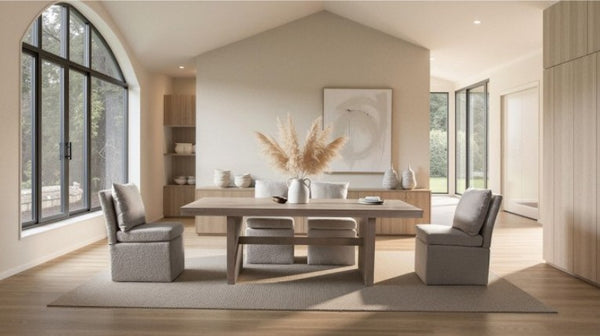 Montague Cross Modern Style Rectangular Dining Table A modern dining room featuring a light wood rectangular table with four upholstered gray chairs, set on a large beige area rug. The room has a high vaulted ceiling, large arched windows with black frames, and light wood flooring.