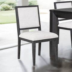 Montague Cross Modern Style Weathered Black Dining Chair Dining chair with white cushioned seat and backrest in a room with a table and window.