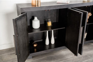 Montague Cross Modern Style Weathered Black Dining Server A dark wood sideboard cabinet with two doors open, showing shelves with decorative white vases and a candle. The cabinet is set against a white wall on a gray wood-look floor.