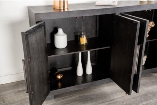 Montague Cross Modern Style Weathered Black Dining Server A dark wood sideboard cabinet with two doors open, showing shelves with decorative white vases and a candle. The cabinet is set against a white wall on a gray wood-look floor.