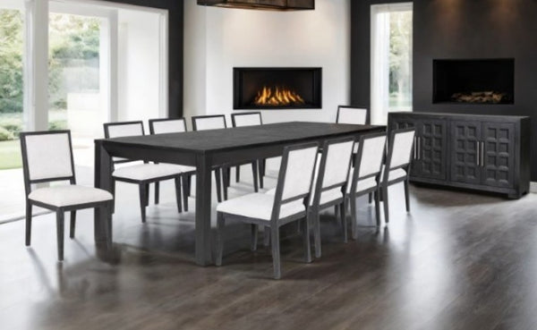 Montague Cross Modern Style Weathered Black Dining Server A modern dining room set featuring a dark gray rectangular dining table and eight matching chairs with white upholstered seats, shown in a contemporary dining room with wood floors and built-in fireplaces.