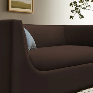 Natalia Chocolate Brown Velvet Fabric Loveseat Brown sofa with a light blue pillow in a room with a framed picture and plant.