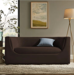 Natalia Chocolate Brown Velvet Fabric Loveseat Brown sofa with a blue pillow in a living room setting with a painting and lamp.