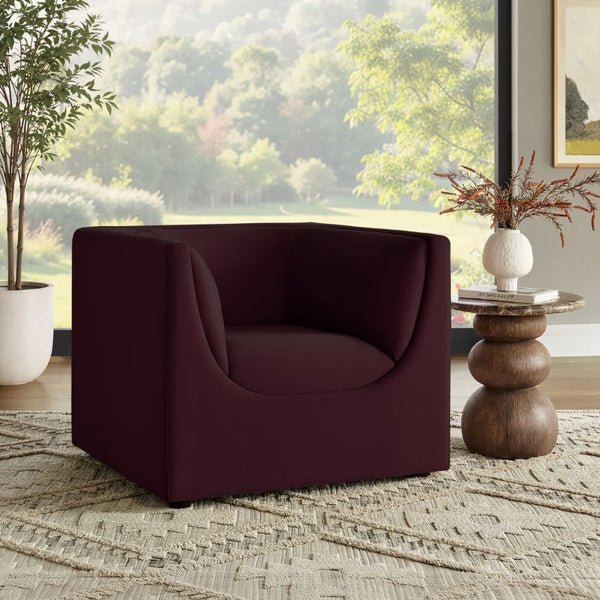 Natalia Mulberry Velvet Fabric Chair Maroon armchair in a room with a wooden side table and decorative elements.