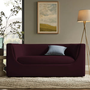 Natalia Mulberry Velvet Fabric Loveseat Maroon sofa in a living room with a painting and lamp in the background