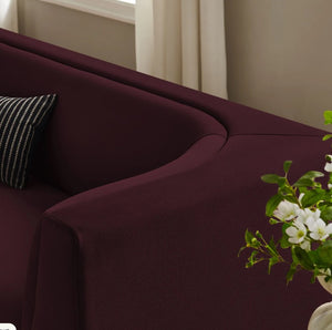 Natalia Mulberry Velvet Fabric Sofa Maroon sofa with a striped pillow and a vase of flowers in a room.