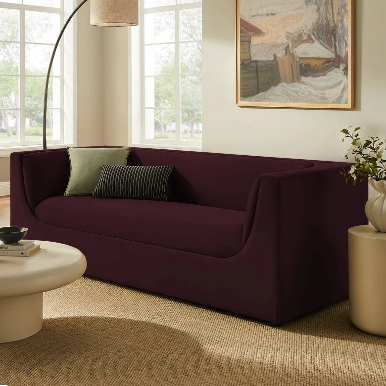 Natalia Mulberry Velvet Fabric Sofa Maroon sofa in a living room with a painting on the wall and a lamp.