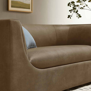 Natalia Premium Vegan Leather Loveseat Brown sofa with a light blue pillow in a room with a framed picture and plant.
