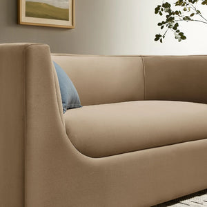 Natalia Taupe Velvet Fabric Loveseat Beige sofa with a blue pillow in a room with a painting and plant on the wall.