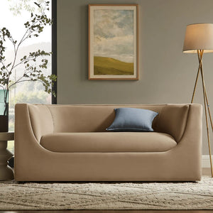 Natalia Taupe Velvet Fabric Loveseat Beige sofa with a blue pillow in a living room setting with a painting and lamp.