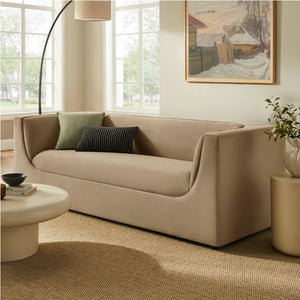 Natalia Taupe Velvet Fabric Sofa Beige sofa in a living room with a painting on the wall and a plant on a side table.