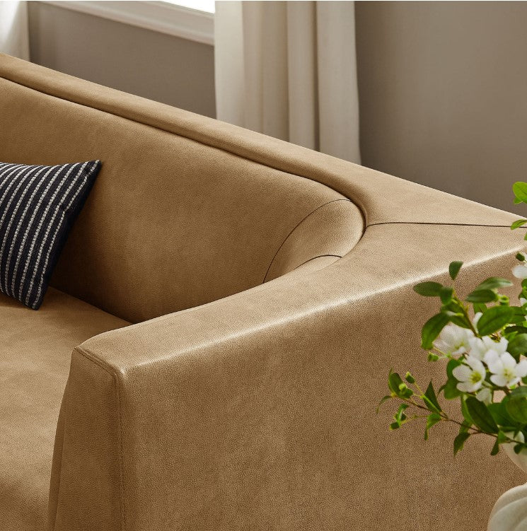 Natalia Toast Premium Vegan Leather Sofa Beige sofa in a living room with a painting on the wall and a plant on a side table.