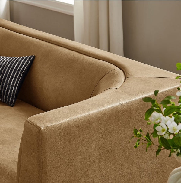 Natalia Toast Premium Vegan Leather Sofa Brown sofa with a striped pillow and a plant in a room with neutral decor.