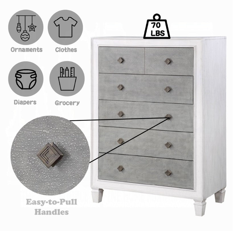 Natasha Two Tone Light Gray Chest A white five-drawer chest of drawers with textured gray front panels stands in a bedroom setting against a light gray wall, with a bed and white curtain partially visible on the right.