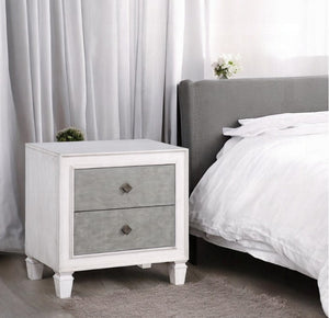 Natasha Two Tone Light Gray Nightstand A white two-drawer nightstand with textured gray drawer fronts and dark metal knobs, positioned next to a bed with white linens and a gray headboard in a softly lit bedroom.