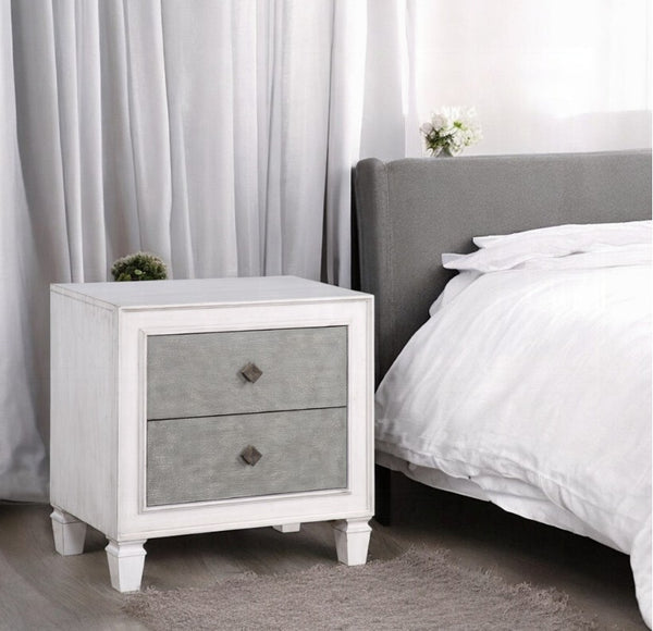 Natasha Two Tone Light Gray Nightstand A white two-drawer nightstand with textured gray drawer fronts and dark metal knobs, positioned next to a bed with white linens and a gray headboard in a softly lit bedroom.