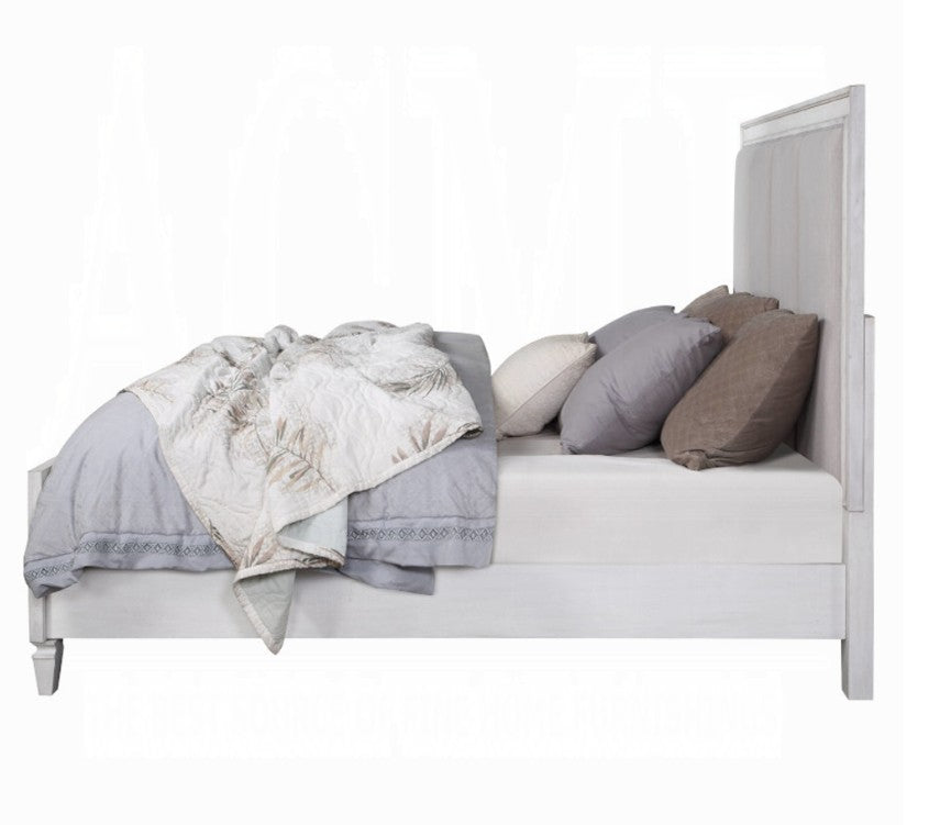 Natasha Upholstered Light Gray Linen Bedroom A bedroom furniture set in a staged room, featuring a white and gray upholstered bed frame, matching dresser, nightstand, and chest of drawers, with a gray rug and gray walls.
