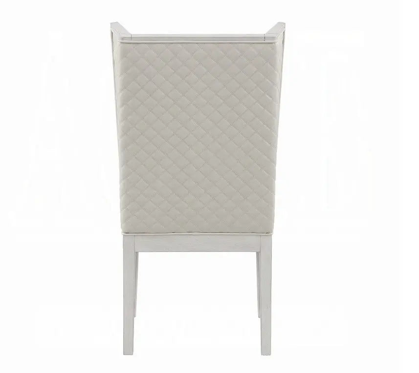 A white dining chair with a light gray upholstered seat and backrest, positioned on a gray and white patterned rug in a bright room with sheer curtains and windows.
