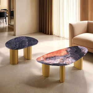 Naynem Coffee Table Oval Sintered Stone Black Gray Gold Finish Two modern oval coffee tables with gold-finished cylindrical legs and marbled stone tops, shown in a styled living room setting with a beige sofa and curtains.