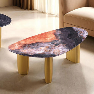 Naynem Coffee Table Oval Sintered Stone Black Gray Gold Finish An abstract-shaped coffee table with a marbled top in orange, black, and gray, supported by three cylindrical gold legs, shown in a modern living room setting.