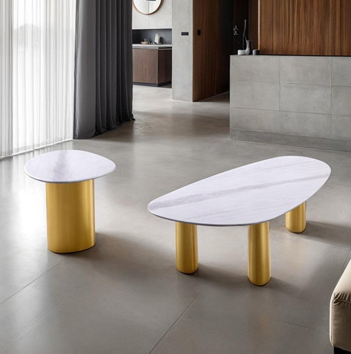 Naynem Coffee Table Oval Sintered Stone White Gold Finish An oval coffee table with a white marble-look top and four cylindrical gold legs, shown in a modern interior setting with a concrete floor and gray tiled wall.