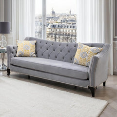 Nikki Gray Button Tufted Sofa Gray sofa with patterned cushions in a room with large windows showing an urban view.