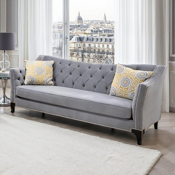 Nikki Gray Button Tufted Sofa Gray sofa with patterned cushions in a room with large windows showing an urban view.