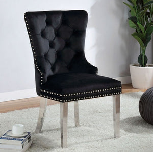 Noonwit Chrome Black Flannelette Fabric Chair (2/PK) A black tufted velvet dining chair with silver nailhead trim and tapered silver metal legs, shown in a styled room setting on a white rug with a potted plant and books in the background.